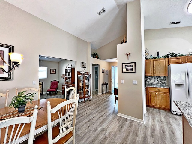 kitchen featuring lofted ceiling, white fridge with ice dispenser, backsplash, and light hardwood / wood-style flooring