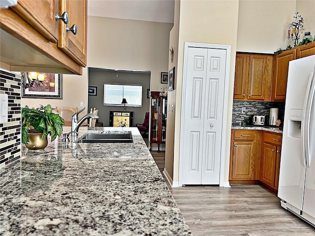 kitchen with an inviting chandelier, sink, white fridge with ice dispenser, tasteful backsplash, and light stone counters