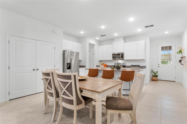 kitchen with stainless steel appliances, an island with sink, light tile patterned floors, and white cabinets