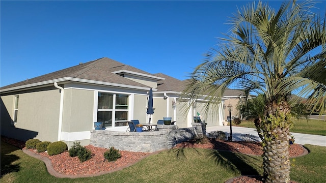 1881 Sassparilla Way, The Villages, FL 32162 - rear view of property featuring concrete driveway, a lawn, a shingled roof, stucco siding, and a patio area
