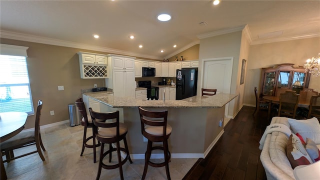 kitchen featuring white cabinets, vaulted ceiling, light stone counters, and black appliances