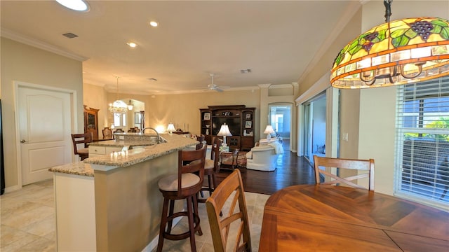 kitchen featuring pendant lighting, ceiling fan with notable chandelier, light stone counters, and ornamental molding