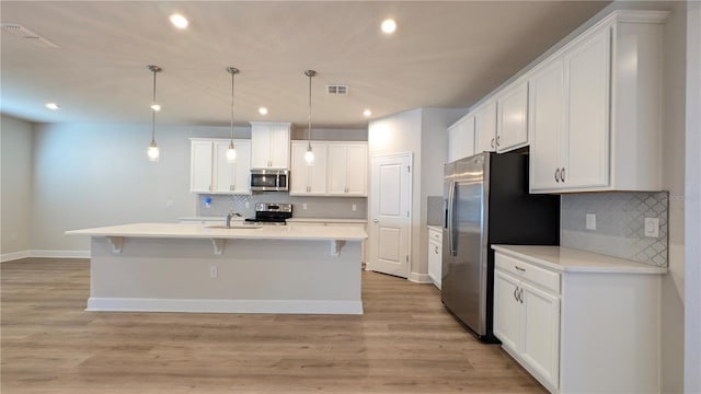 kitchen with a kitchen island with sink, white cabinets, stainless steel appliances, and decorative light fixtures