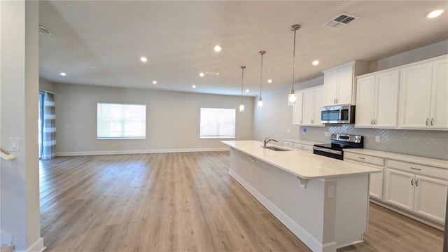 kitchen with pendant lighting, a kitchen island with sink, white cabinets, sink, and appliances with stainless steel finishes