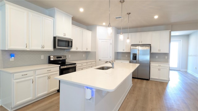 kitchen featuring sink, stainless steel appliances, pendant lighting, a kitchen island with sink, and white cabinets