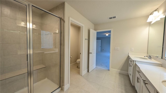 bathroom featuring tile patterned flooring, vanity, toilet, and a shower with shower door