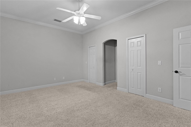 unfurnished bedroom featuring carpet, ceiling fan, crown molding, and multiple closets