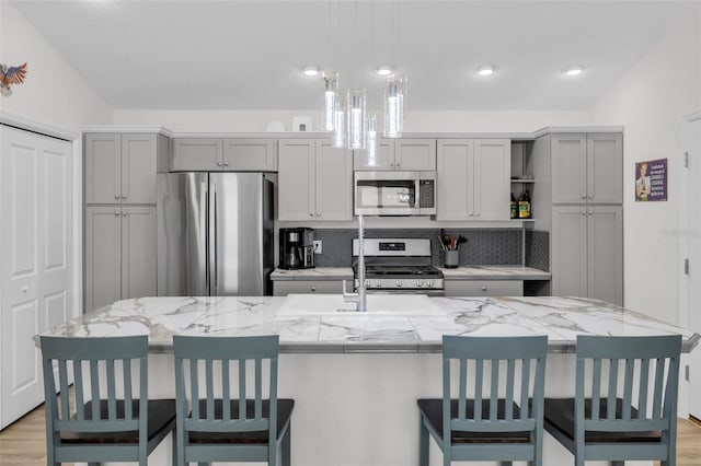 kitchen with tasteful backsplash, gray cabinets, a large island with sink, and appliances with stainless steel finishes