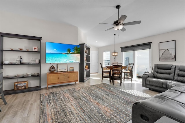 living room with ceiling fan with notable chandelier, light hardwood / wood-style floors, and vaulted ceiling