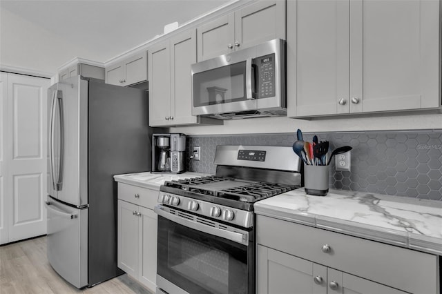 kitchen featuring light stone counters, light wood-type flooring, backsplash, and appliances with stainless steel finishes