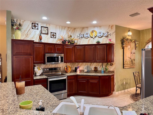 kitchen with light stone counters, sink, stainless steel appliances, and a textured ceiling