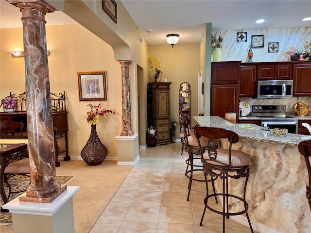 kitchen featuring decorative columns, light colored carpet, stainless steel appliances, and a breakfast bar area