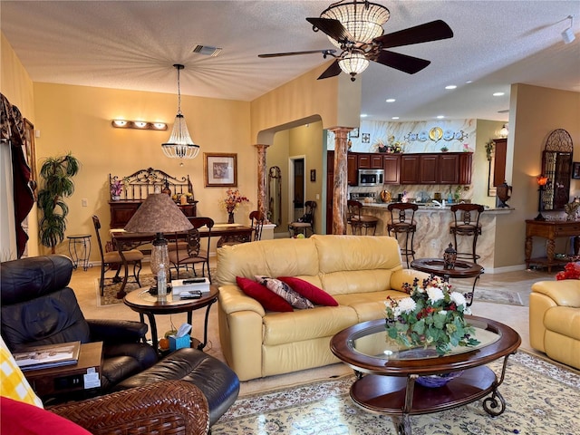 living room with ceiling fan, a textured ceiling, and decorative columns