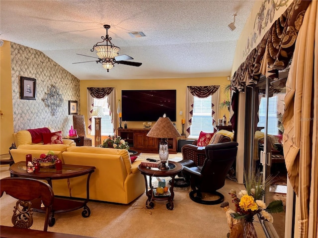 carpeted living area with visible vents, an accent wall, ceiling fan, wallpapered walls, and a textured ceiling
