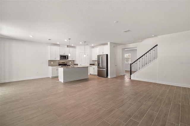 kitchen with white cabinetry, appliances with stainless steel finishes, pendant lighting, and a center island with sink