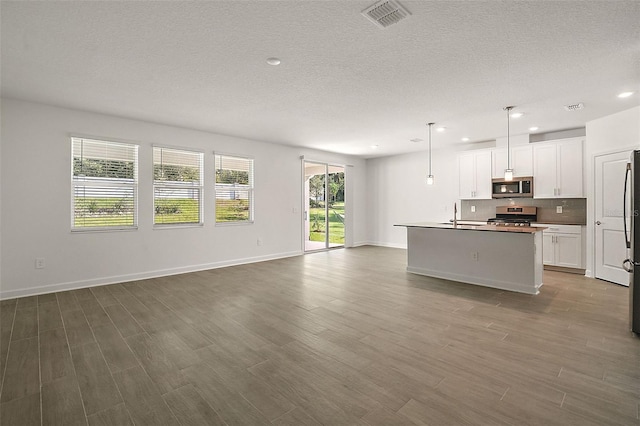 kitchen with white cabinetry, wood-type flooring, decorative light fixtures, appliances with stainless steel finishes, and an island with sink