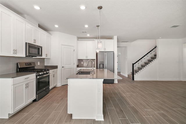 kitchen with sink, appliances with stainless steel finishes, white cabinetry, a center island with sink, and decorative light fixtures