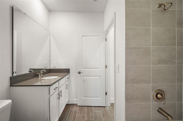 full bathroom featuring tiled shower / bath combo, vanity, a textured ceiling, and toilet