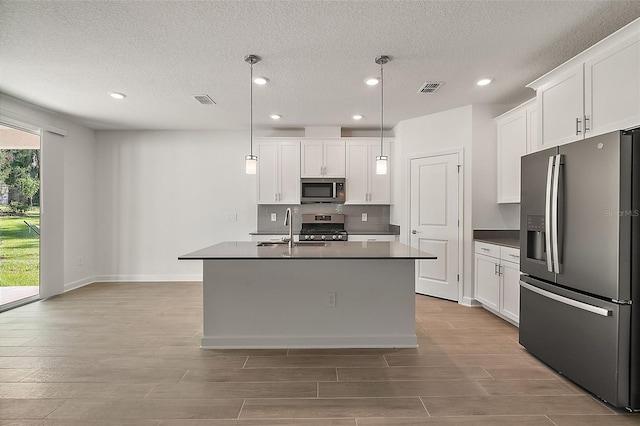 kitchen with stainless steel appliances, an island with sink, and white cabinets