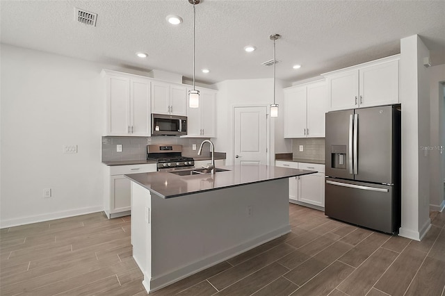 kitchen featuring sink, stainless steel appliances, white cabinets, a center island with sink, and decorative light fixtures