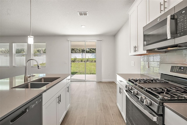 kitchen with pendant lighting, sink, white cabinets, and appliances with stainless steel finishes