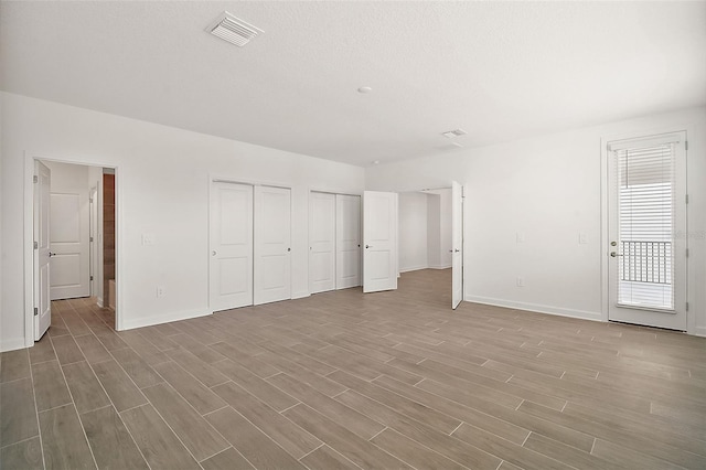 unfurnished bedroom with two closets, access to exterior, a textured ceiling, and light hardwood / wood-style flooring