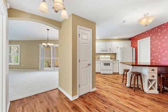 kitchen with pendant lighting, white appliances, an inviting chandelier, a kitchen bar, and white cabinetry