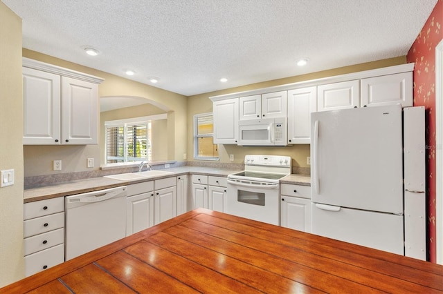 kitchen with a textured ceiling, white cabinetry, sink, and white appliances