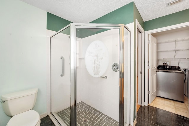 bathroom with washer / dryer, tile patterned flooring, a textured ceiling, toilet, and a shower with shower door