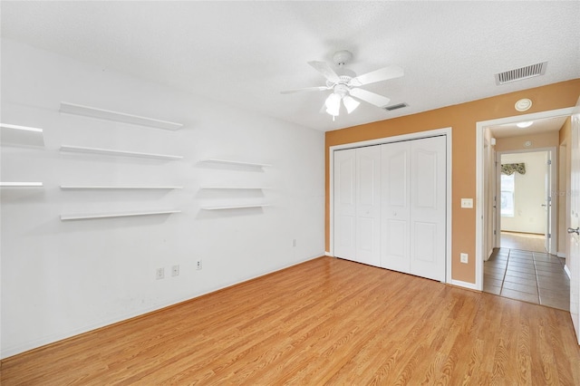 unfurnished bedroom with ceiling fan, a closet, a textured ceiling, and light wood-type flooring