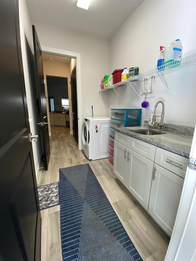 clothes washing area with sink, independent washer and dryer, and light wood-type flooring