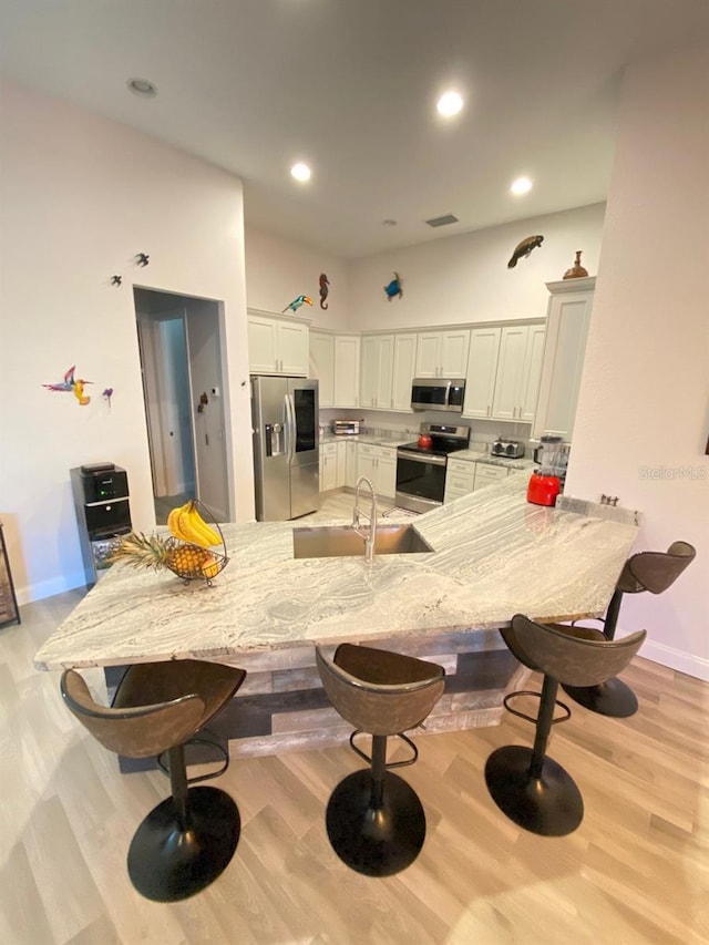 kitchen featuring sink, light stone counters, kitchen peninsula, stainless steel appliances, and white cabinets