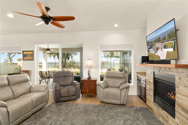 living room featuring light hardwood / wood-style floors, a stone fireplace, and ceiling fan