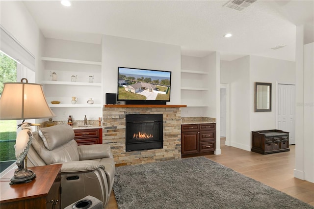 living room featuring built in shelves, light hardwood / wood-style floors, and a stone fireplace