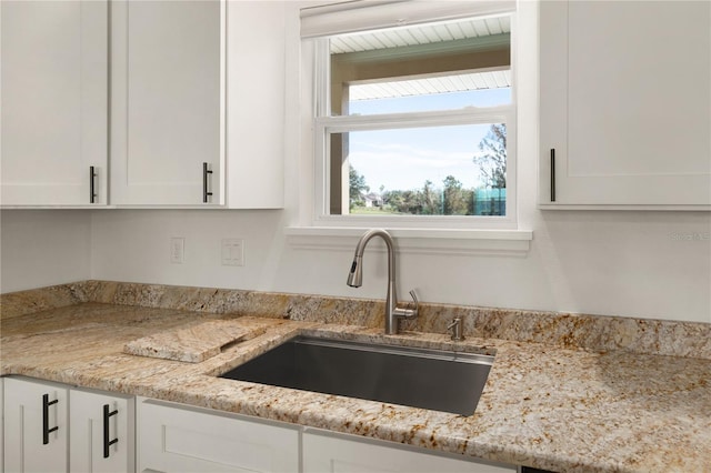 kitchen with white cabinets, light stone countertops, and sink