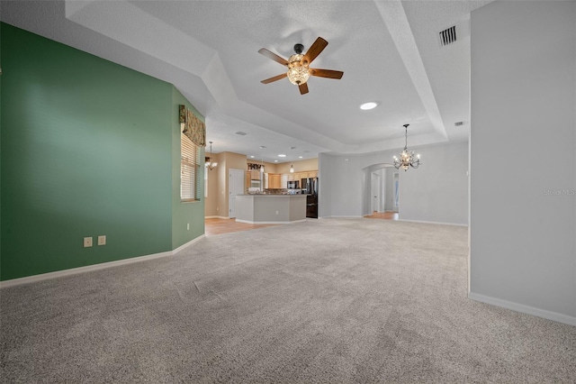 unfurnished living room featuring ceiling fan with notable chandelier, a tray ceiling, visible vents, and baseboards