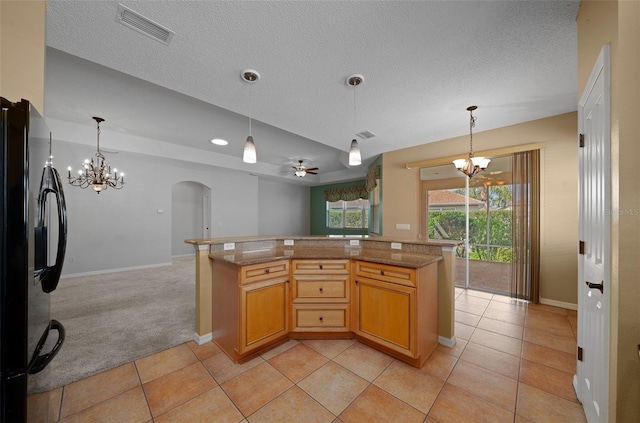 kitchen featuring visible vents, arched walkways, open floor plan, decorative light fixtures, and freestanding refrigerator