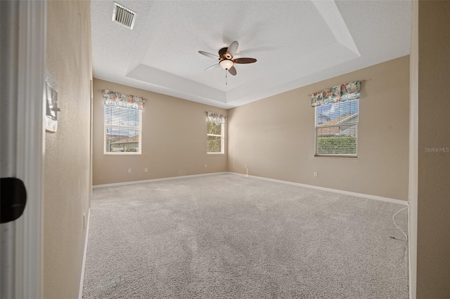 empty room with carpet, a raised ceiling, visible vents, a textured ceiling, and baseboards