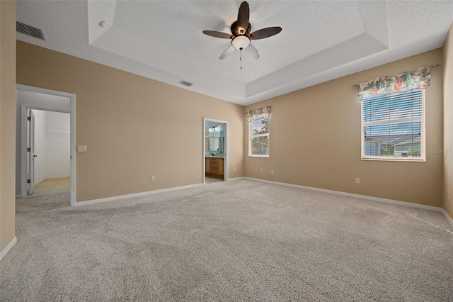 empty room with visible vents, a raised ceiling, a textured ceiling, and light colored carpet