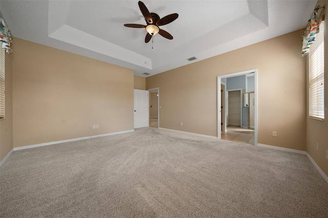 interior space featuring light carpet, baseboards, visible vents, a raised ceiling, and a ceiling fan