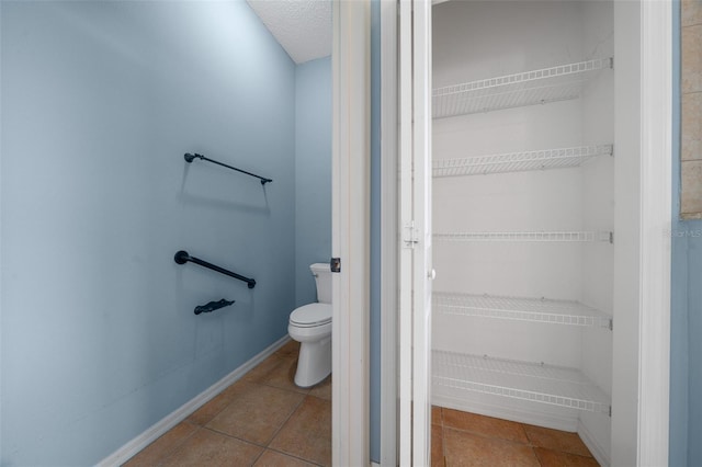 bathroom with baseboards, a textured ceiling, toilet, and tile patterned floors