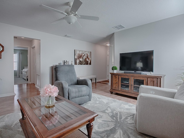 living room with ceiling fan, a textured ceiling, and light hardwood / wood-style flooring