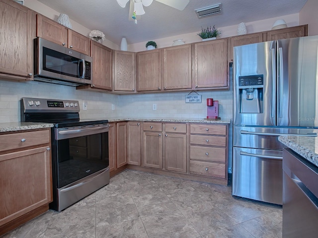 kitchen featuring light stone countertops, a textured ceiling, appliances with stainless steel finishes, and tasteful backsplash