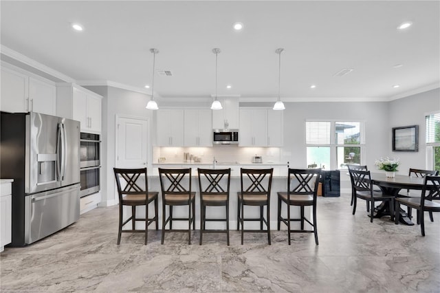 kitchen with white cabinets, stainless steel appliances, hanging light fixtures, and an island with sink