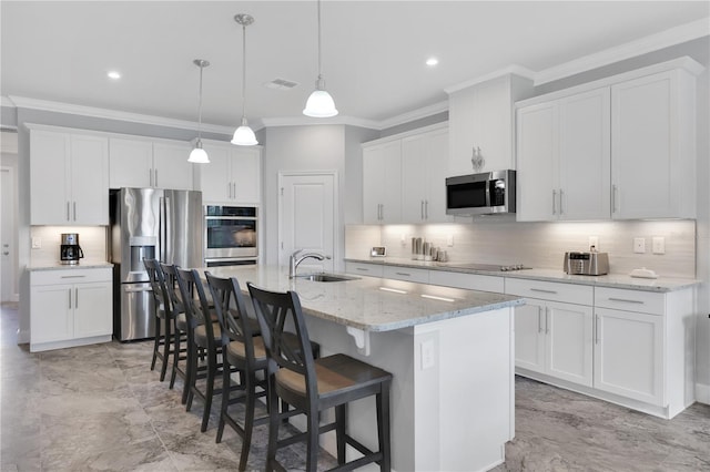 kitchen featuring stainless steel appliances, sink, white cabinetry, hanging light fixtures, and an island with sink