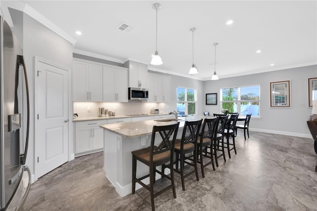 kitchen featuring a kitchen island with sink, white cabinets, hanging light fixtures, appliances with stainless steel finishes, and light stone counters