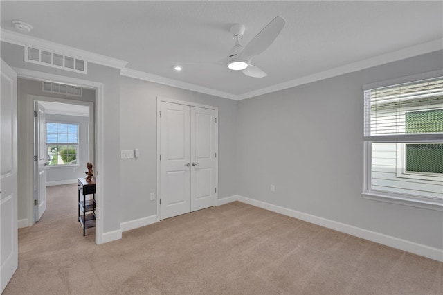 unfurnished bedroom featuring ceiling fan, a closet, light carpet, and ornamental molding