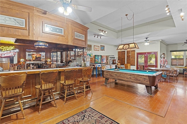 game room featuring french doors, a raised ceiling, wooden walls, indoor bar, and pool table