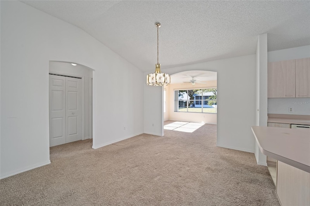 unfurnished dining area featuring a textured ceiling, ceiling fan with notable chandelier, lofted ceiling, and light colored carpet