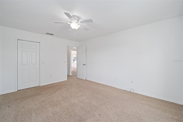 unfurnished bedroom with ceiling fan, a textured ceiling, a closet, and light carpet